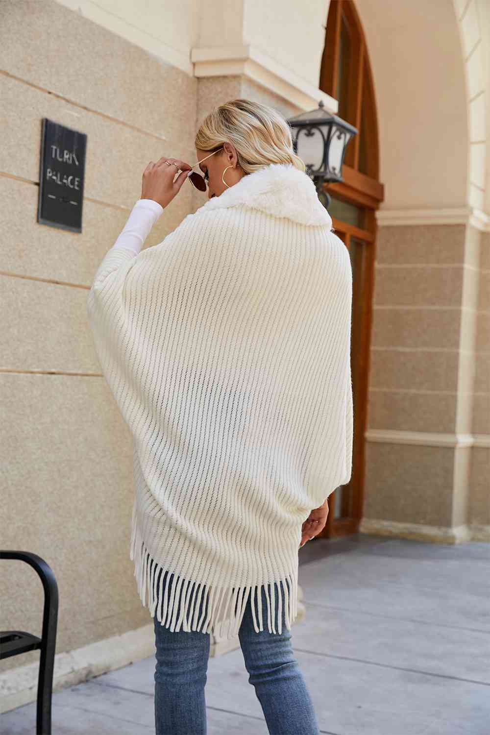 Back of model wearing ivory open front poncho with fringe and faux fur trim