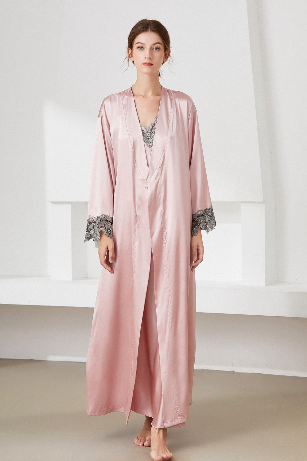 Woman standing wearing pink satin nightdress and matching robe with lace trim