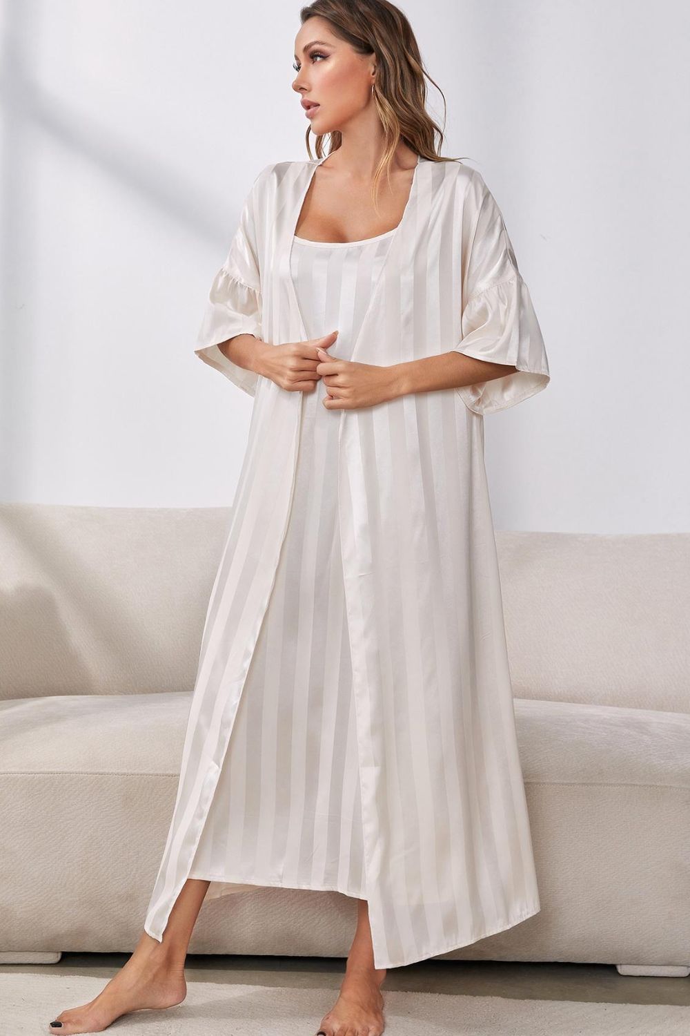 Woman standing in front of sofa wearing beige striped nightgown and matching beige striped robe