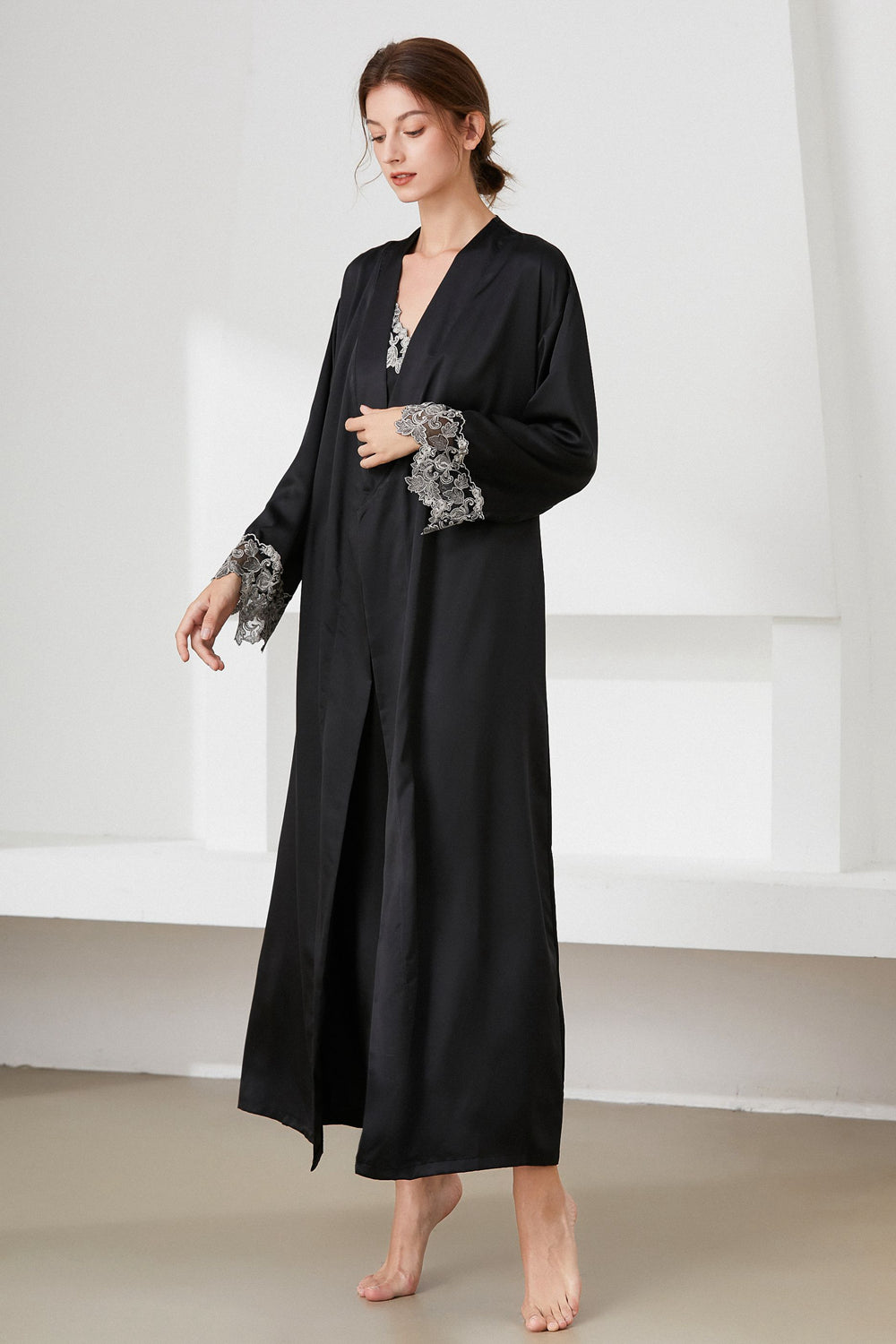 Angle view of woman standing wearing black satin nightdress and matching robe, with lace trim
