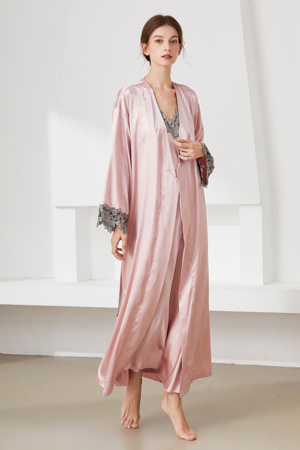 Angle view of woman standing wearing pink  nightdress and matching robe, with lace trim