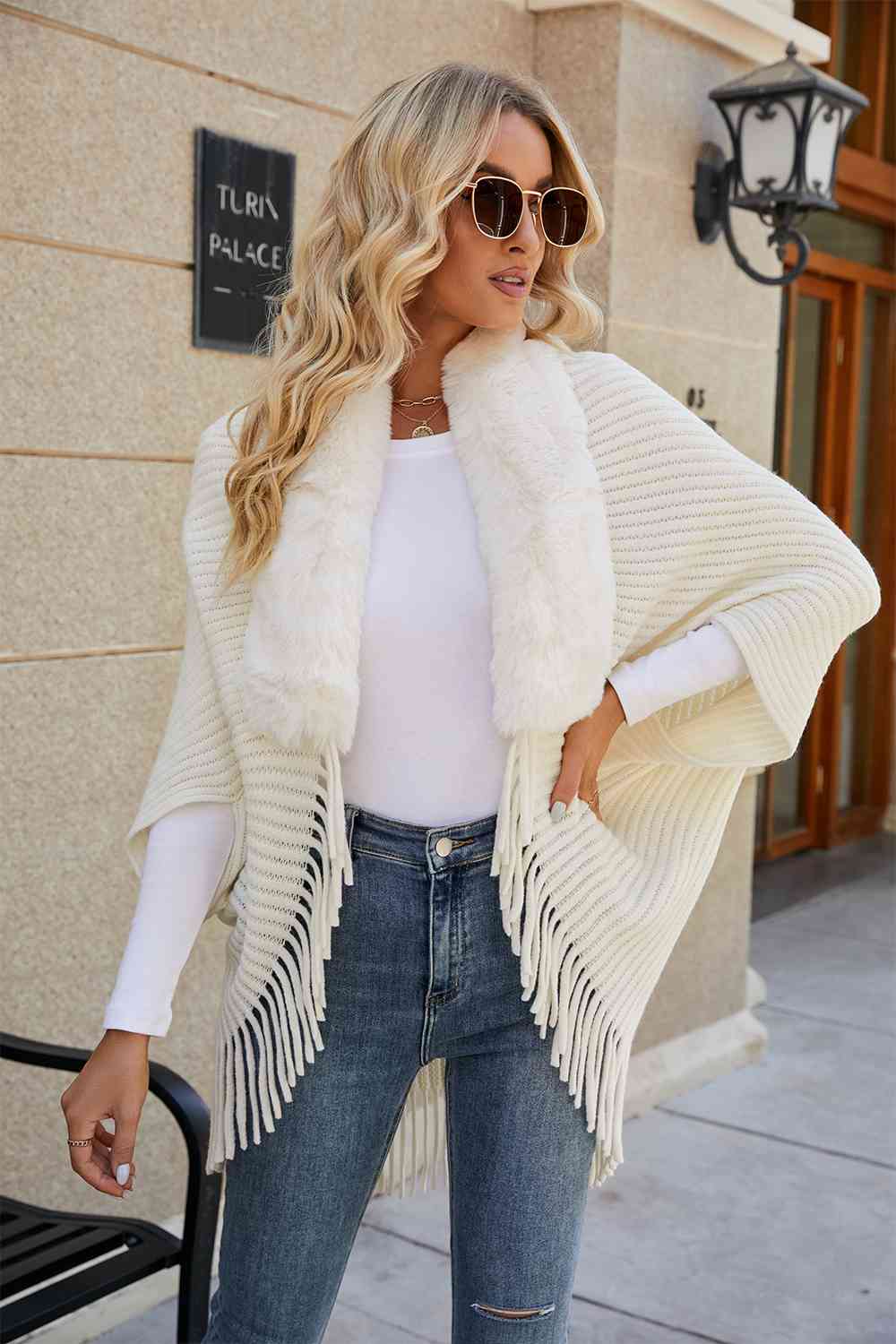 Model wearing ivory open front poncho with fringe and faux fur trim